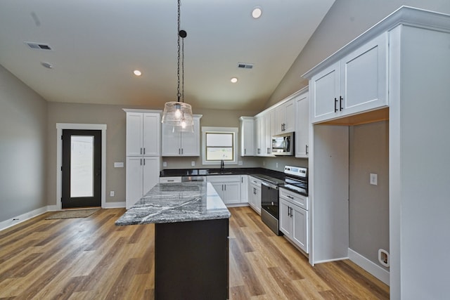 kitchen featuring appliances with stainless steel finishes, vaulted ceiling, decorative light fixtures, white cabinets, and a center island