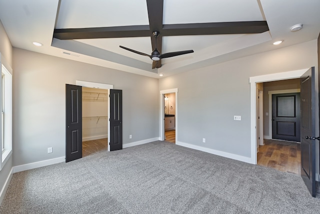 unfurnished bedroom featuring dark colored carpet, a raised ceiling, a walk in closet, ceiling fan, and a closet