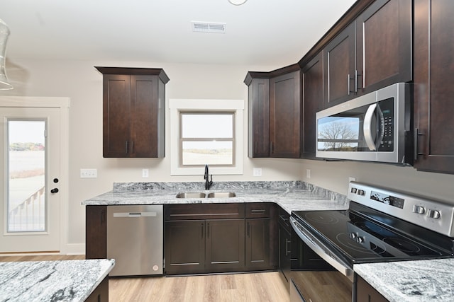 kitchen featuring sink, light wood-type flooring, appliances with stainless steel finishes, light stone counters, and dark brown cabinetry