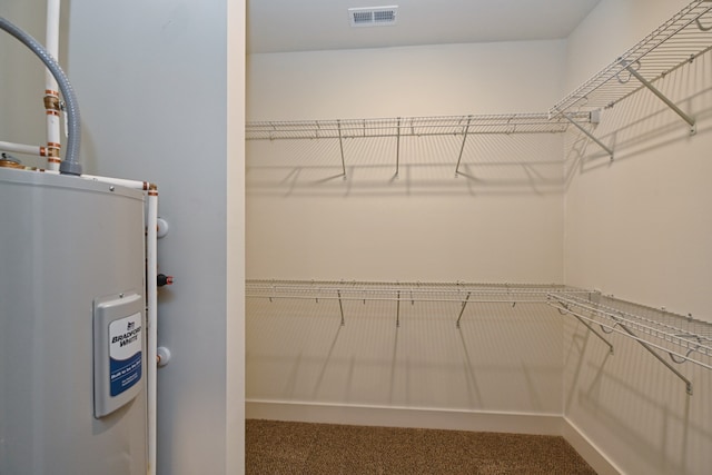 spacious closet featuring electric water heater and carpet floors