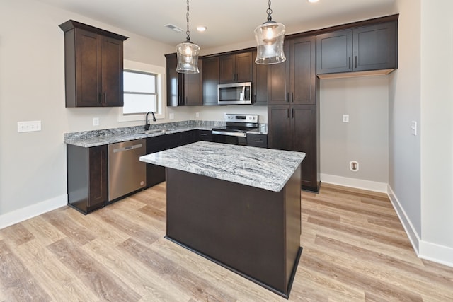 kitchen with light stone countertops, stainless steel appliances, pendant lighting, a center island, and light hardwood / wood-style floors