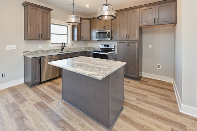 kitchen with pendant lighting, sink, light wood-type flooring, a kitchen island, and stainless steel appliances