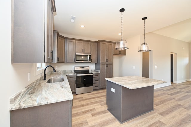 kitchen with appliances with stainless steel finishes, sink, light hardwood / wood-style floors, a kitchen island, and hanging light fixtures