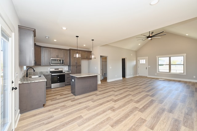 kitchen featuring stainless steel appliances, pendant lighting, lofted ceiling, a kitchen island, and light wood-type flooring