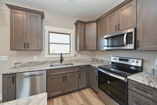 kitchen featuring dark brown cabinetry, sink, stainless steel appliances, light stone counters, and light hardwood / wood-style flooring