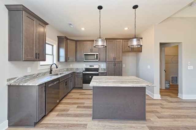 kitchen with sink, light stone countertops, decorative light fixtures, a kitchen island, and stainless steel appliances