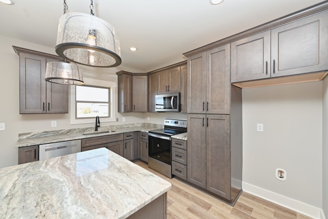 kitchen featuring light stone countertops, sink, light hardwood / wood-style flooring, pendant lighting, and appliances with stainless steel finishes