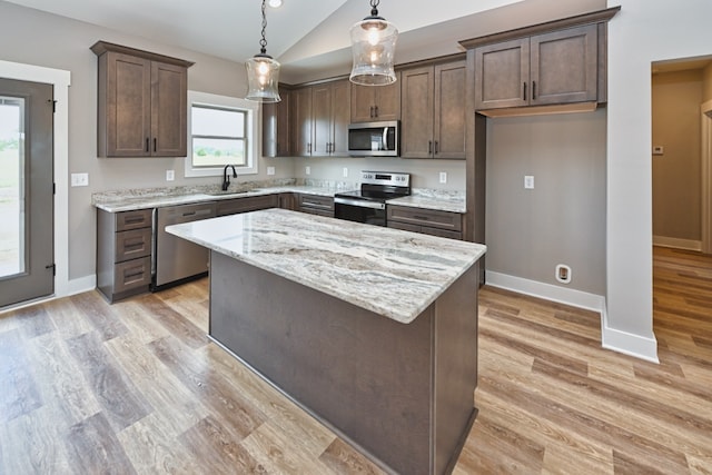 kitchen featuring light stone counters, stainless steel appliances, sink, decorative light fixtures, and a kitchen island