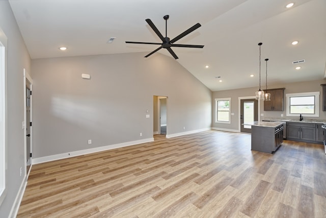 kitchen with high vaulted ceiling, ceiling fan with notable chandelier, light wood-type flooring, decorative light fixtures, and a kitchen island