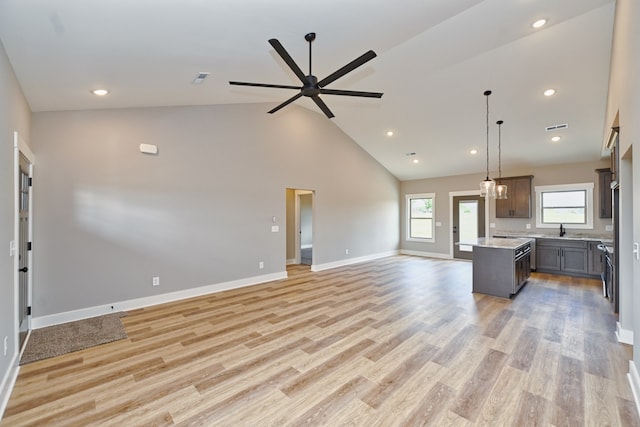 kitchen featuring ceiling fan with notable chandelier, high vaulted ceiling, light hardwood / wood-style flooring, a kitchen island, and hanging light fixtures