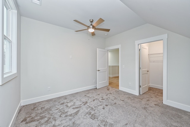 unfurnished bedroom featuring light carpet, a walk in closet, ceiling fan, a closet, and lofted ceiling