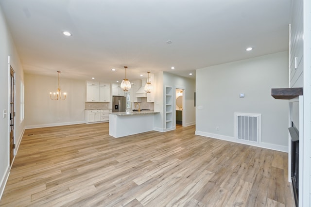 unfurnished living room with an inviting chandelier, light hardwood / wood-style flooring, and sink