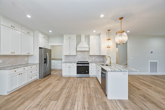 kitchen with white cabinets, appliances with stainless steel finishes, premium range hood, and decorative light fixtures