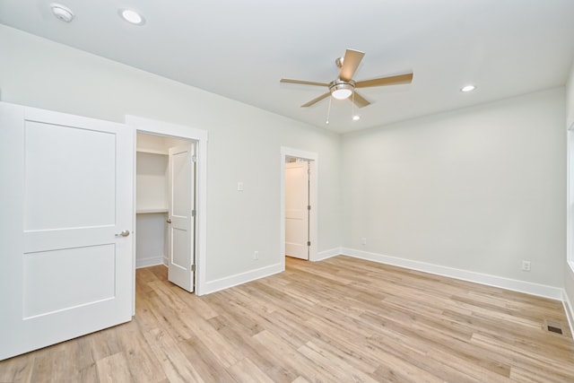 unfurnished bedroom with a closet, a walk in closet, light hardwood / wood-style floors, and ceiling fan