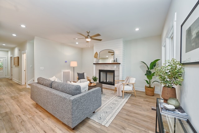 living room with light hardwood / wood-style floors, ceiling fan, and a premium fireplace