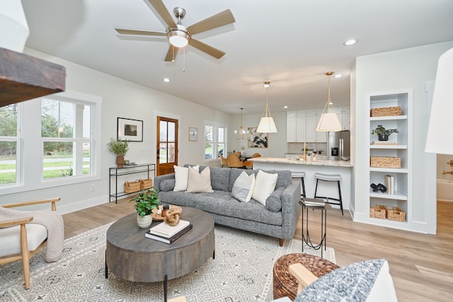 living room with a healthy amount of sunlight, ceiling fan with notable chandelier, and light wood-type flooring