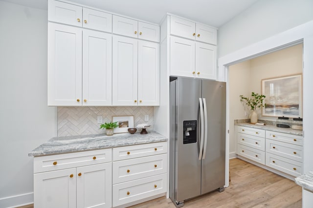 kitchen featuring stainless steel fridge, light wood-type flooring, tasteful backsplash, light stone counters, and white cabinets