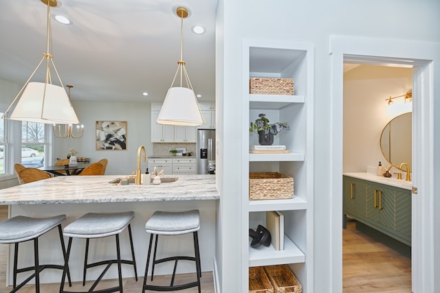 kitchen with white cabinetry, sink, stainless steel fridge with ice dispenser, pendant lighting, and light hardwood / wood-style floors