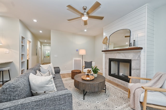 living room with light hardwood / wood-style flooring, ceiling fan, and a premium fireplace