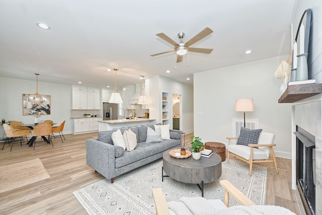 living room featuring ceiling fan with notable chandelier and light wood-type flooring