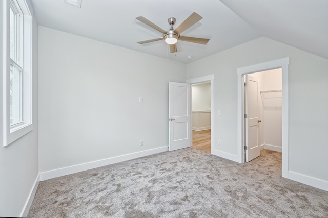 unfurnished bedroom with ceiling fan, light colored carpet, vaulted ceiling, a walk in closet, and a closet