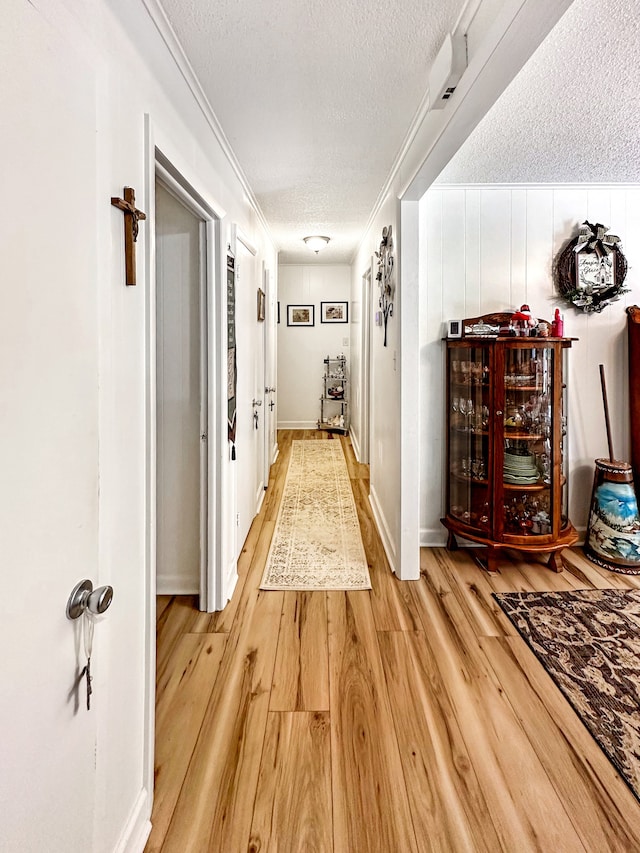 hall with baseboards, a textured ceiling, light wood-style flooring, and crown molding