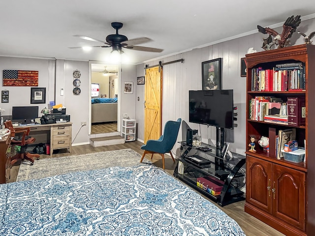 bedroom with ceiling fan, crown molding, a barn door, and wood finished floors