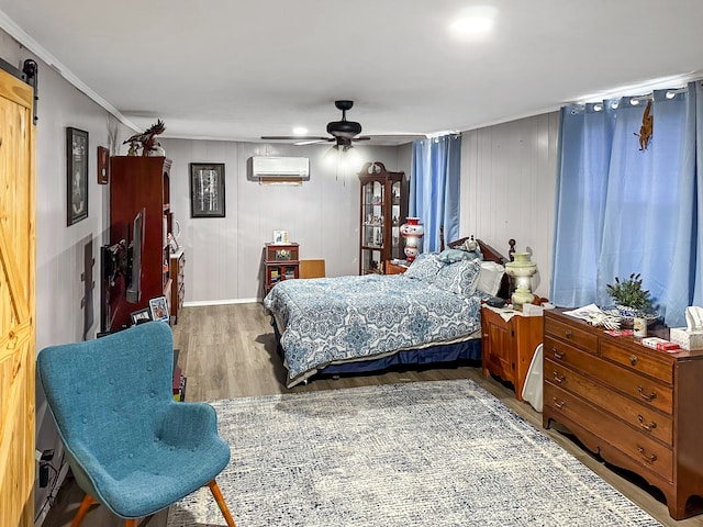 bedroom featuring a wall mounted air conditioner, a ceiling fan, wood finished floors, a barn door, and crown molding