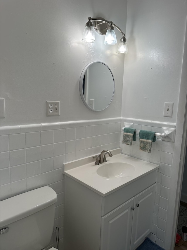 half bathroom featuring wainscoting, toilet, vanity, and tile walls