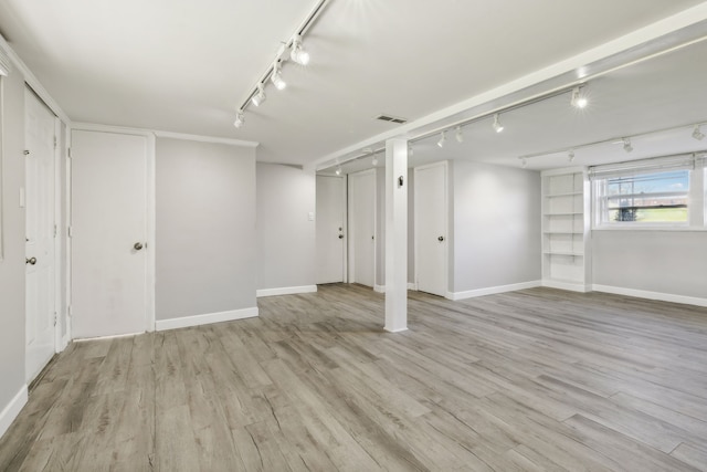 basement with rail lighting and light hardwood / wood-style floors