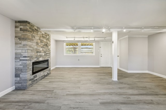 unfurnished living room featuring a stone fireplace, light hardwood / wood-style flooring, and track lighting