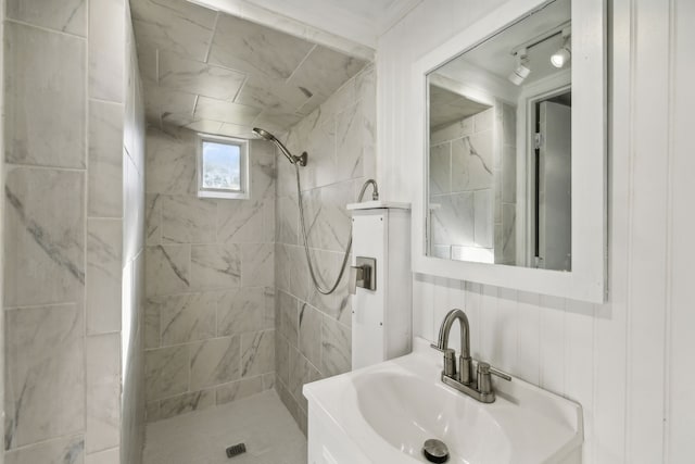 bathroom with a tile shower, ornamental molding, and sink