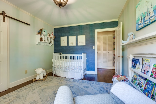 bedroom with a barn door, dark hardwood / wood-style flooring, a nursery area, and ornamental molding