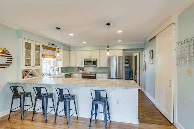 kitchen with hanging light fixtures, kitchen peninsula, light hardwood / wood-style floors, white cabinets, and appliances with stainless steel finishes