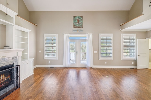 unfurnished living room featuring hardwood / wood-style flooring, a healthy amount of sunlight, a fireplace, and french doors