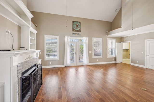 unfurnished living room featuring hardwood / wood-style flooring, high vaulted ceiling, and french doors