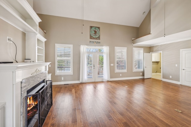 unfurnished living room with hardwood / wood-style floors, high vaulted ceiling, french doors, and a premium fireplace