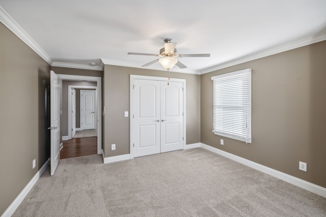 unfurnished bedroom with ceiling fan, light colored carpet, crown molding, and a closet