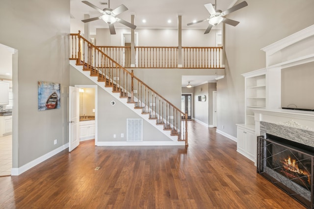 unfurnished living room with ceiling fan, a towering ceiling, dark wood-type flooring, and a premium fireplace