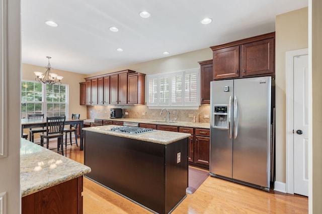 kitchen with appliances with stainless steel finishes, sink, a notable chandelier, a center island, and light hardwood / wood-style floors