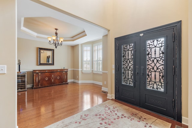 entrance foyer with french doors, a tray ceiling, crown molding, hardwood / wood-style flooring, and an inviting chandelier