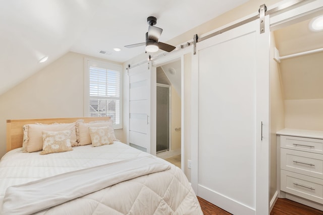 bedroom with a barn door, dark hardwood / wood-style floors, vaulted ceiling, and ceiling fan