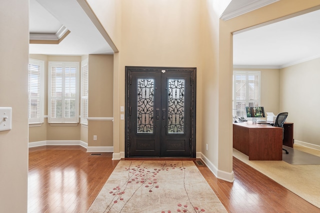 foyer entrance with light hardwood / wood-style floors, ornamental molding, and french doors