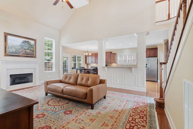 living room with ceiling fan with notable chandelier, light hardwood / wood-style floors, and high vaulted ceiling