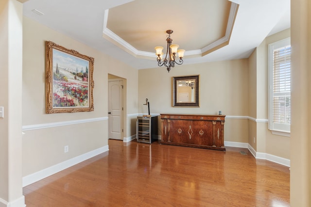 dining space with a notable chandelier, a raised ceiling, crown molding, and light hardwood / wood-style flooring