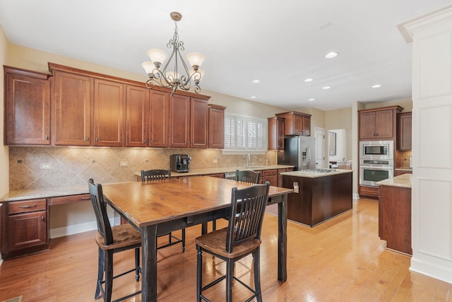 kitchen with appliances with stainless steel finishes, pendant lighting, an inviting chandelier, a center island, and light hardwood / wood-style floors