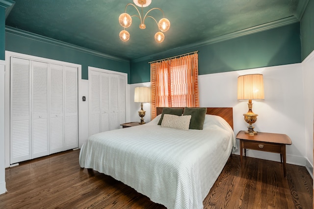 bedroom featuring dark hardwood / wood-style floors, an inviting chandelier, ornamental molding, and two closets