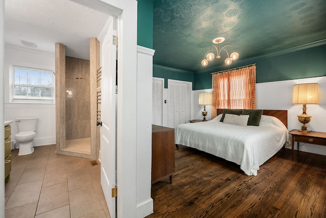 bedroom featuring connected bathroom, multiple closets, an inviting chandelier, crown molding, and wood-type flooring