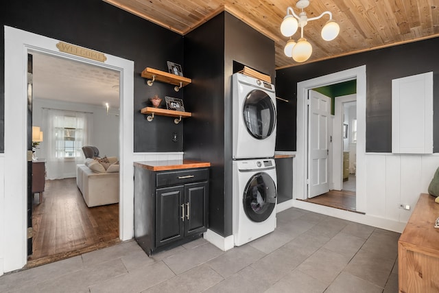 clothes washing area featuring stacked washing maching and dryer, light hardwood / wood-style floors, and wood ceiling