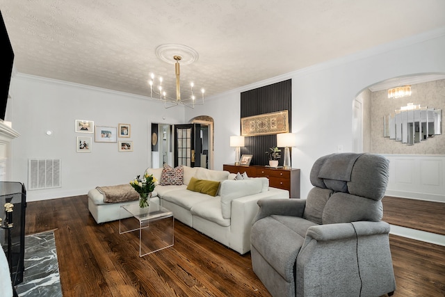 living room with a textured ceiling, dark hardwood / wood-style floors, crown molding, and a notable chandelier